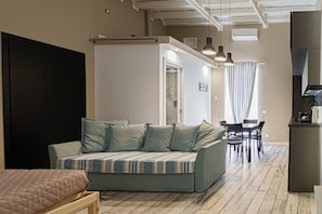 A room with a sofa, a bed, a dining table with chairs, and a kitchenette area. - Cocciu D Amuri Loft by Wonderful Italy (Cefalù)