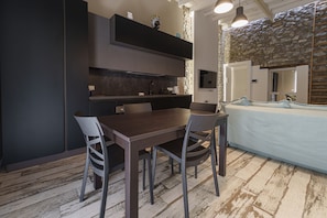A modern kitchen with dark cabinetry, a dining table with chairs, and a stone wall. - Cocciu D Amuri Loft by Wonderful Italy (Cefalù)
