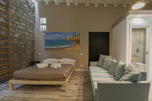 Ein Schlafzimmer mit einem Bett, einer Couch, einer Steinsäule, einem Gemälde und einer Tür zu einem Badezimmer.