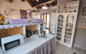 A kitchen with a microwave, kettle, and coffee maker on the counter, a cabinet with dishes, and a painting above the counter. - La Dimora di Max Bright apt. with Terrace (Riposto)