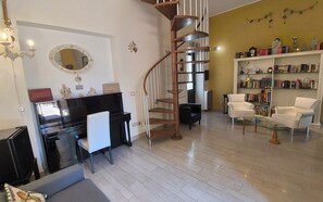 A living room with a piano, a spiral staircase, a bookshelf, and a coffee table. - La Dimora di Max Bright apt. with Terrace (Riposto)