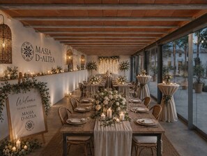 A wedding reception area with a long table set for guests, a sign welcoming to the wedding, and a view of the outdoors through large windows.