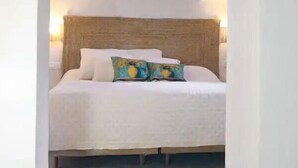 Una cama con cabecera de madera, ropa de cama blanca y un cojín colorido.