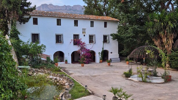 Un edificio blanco con múltiples ventanas y un patio con una fuente y plantas en macetas.