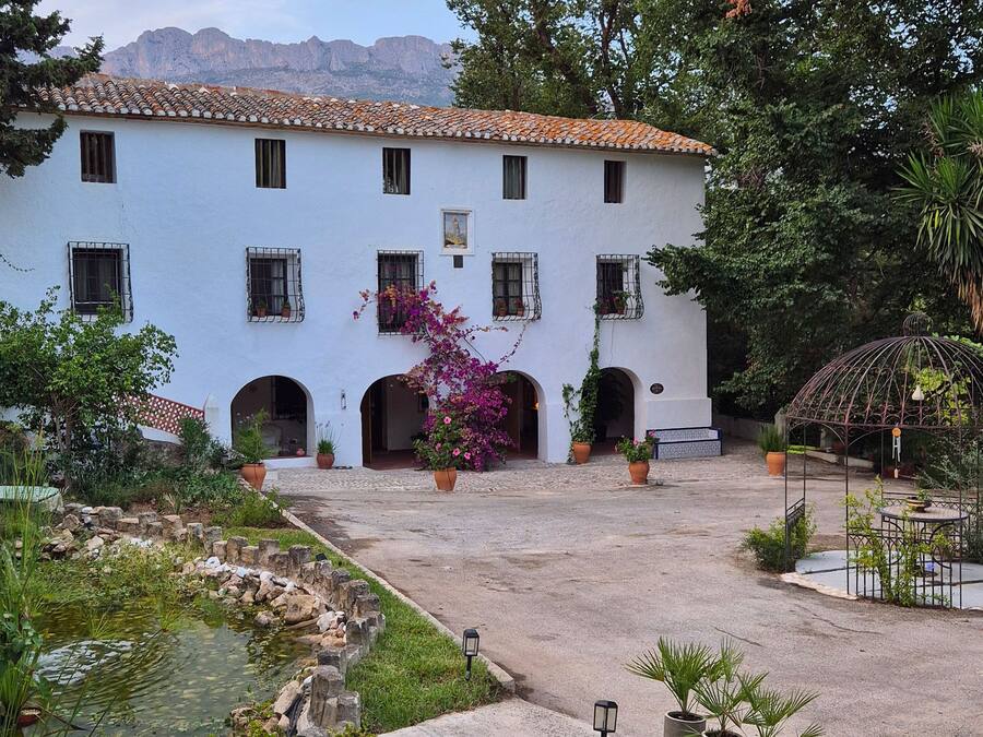 Un edificio blanco con múltiples ventanas y un patio con una fuente y plantas en macetas.