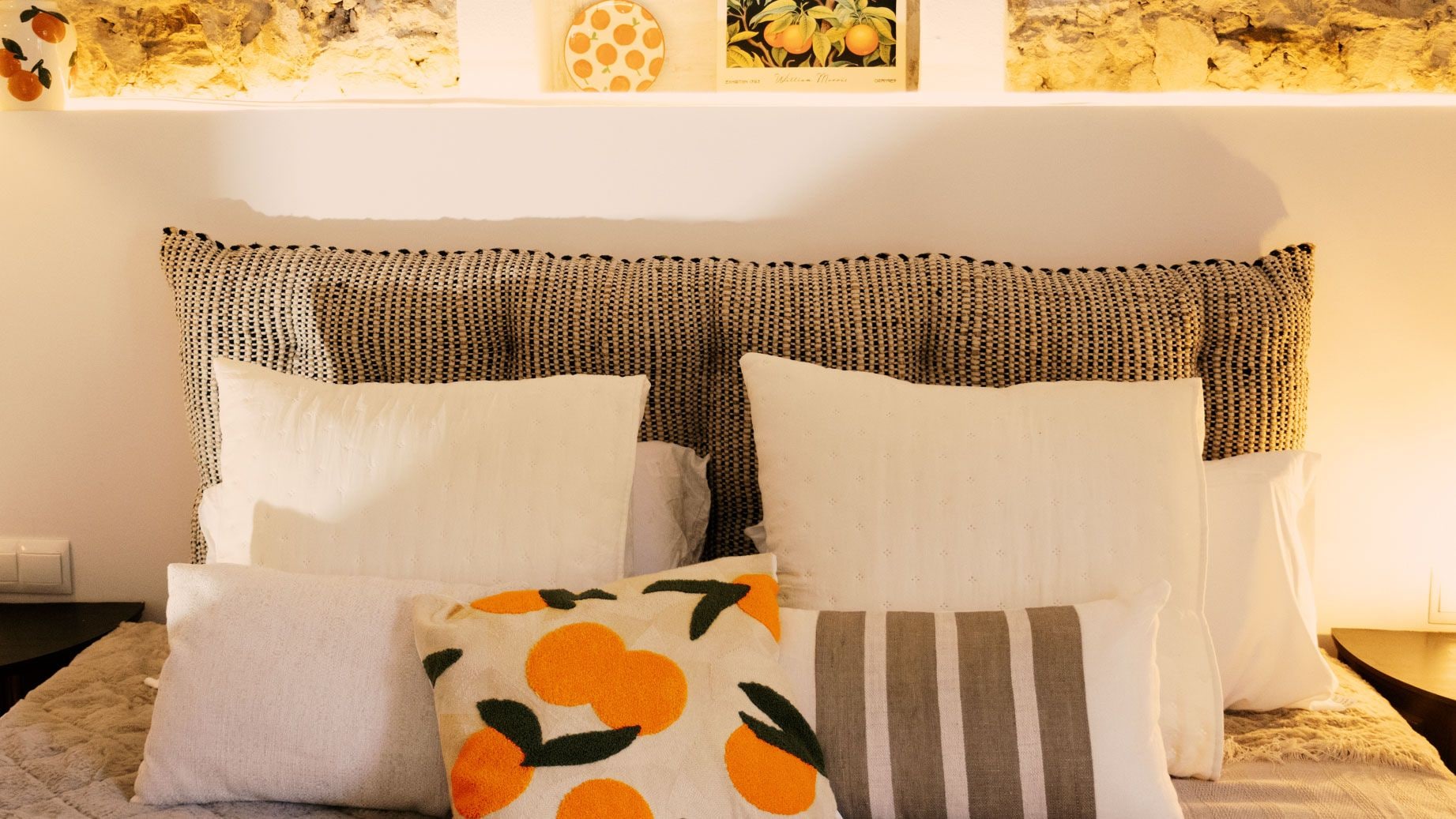 A bed with a patterned headboard, multiple pillows, and a decorative wall above.