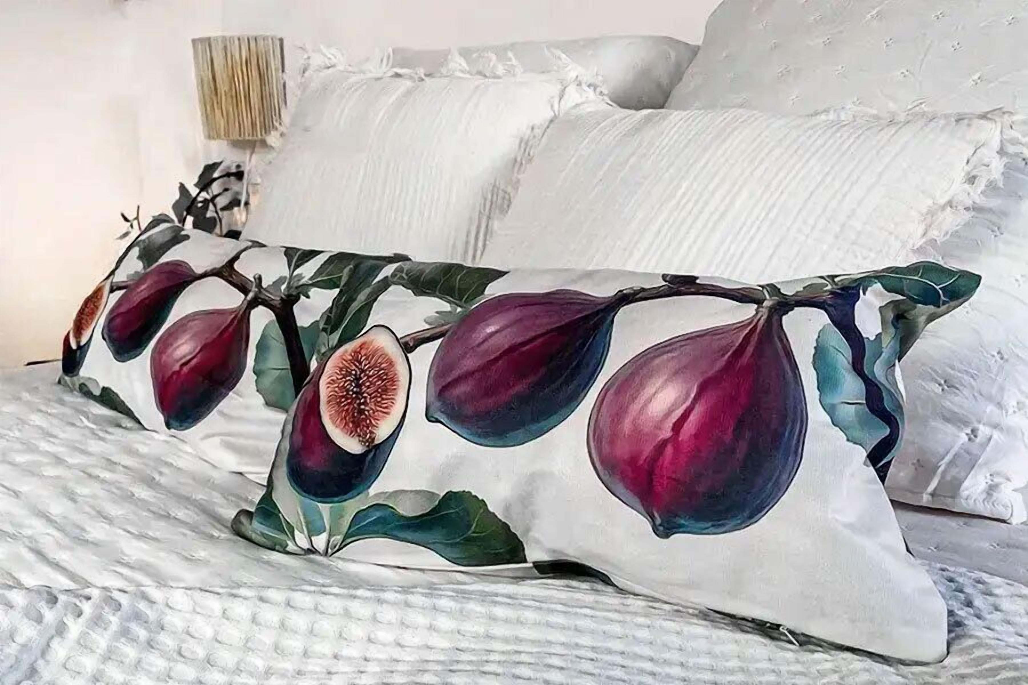 Una cama con ropa blanca y almohadones decorativos con motivos de hojas de higuera.