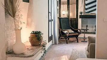 Un interior acogedor con una cama, una silla y una pequeña mesa. Hay una planta en maceta y un jarrón decorativo en un estante.