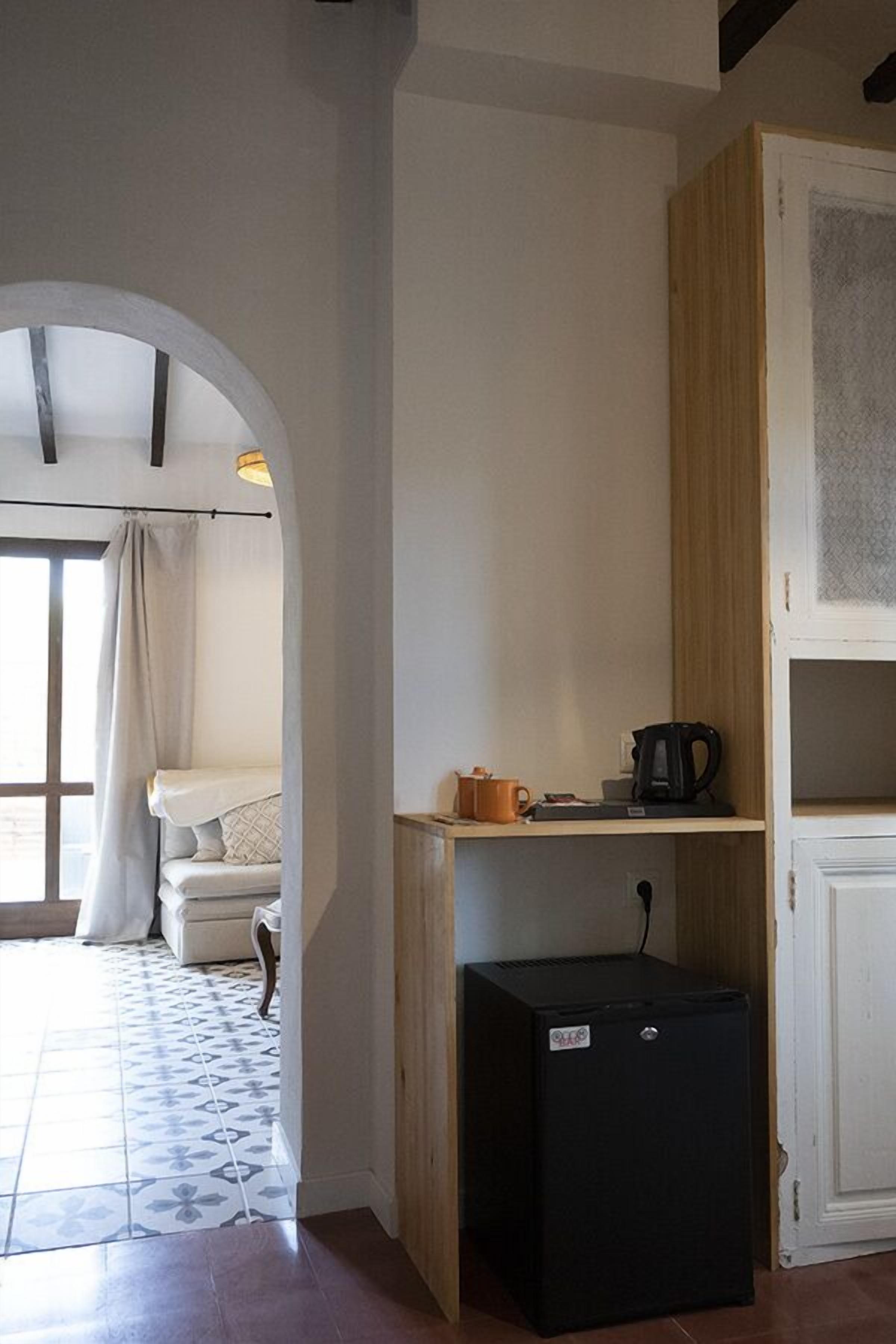 Une pièce compacte dotée d’une kitchenette, d’un petit réfrigérateur et d’une fenêtre avec des rideaux.