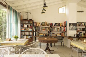 A cozy reading room with a large bookshelf, a round table, and wicker chairs.