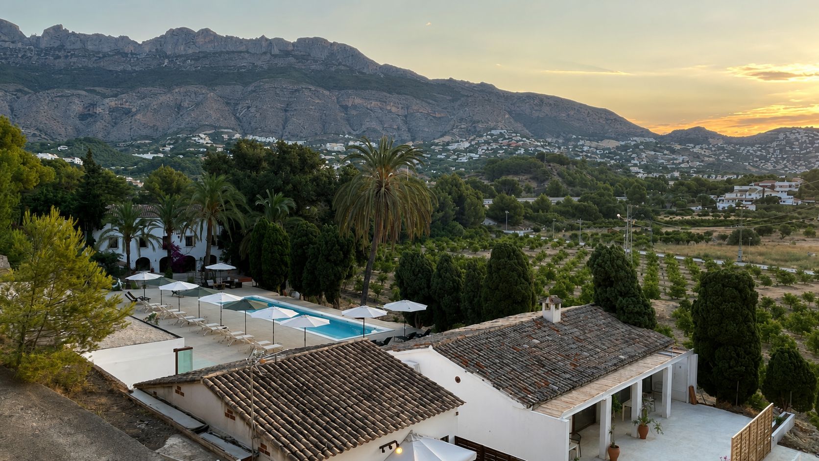 Zona residencial con piscina, edificios blancos y montañas al fondo.