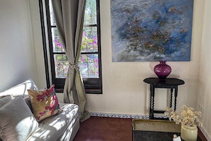 Habitació amb un sofà, una finestra amb cortines, un quadre, un vas i una taula petita.