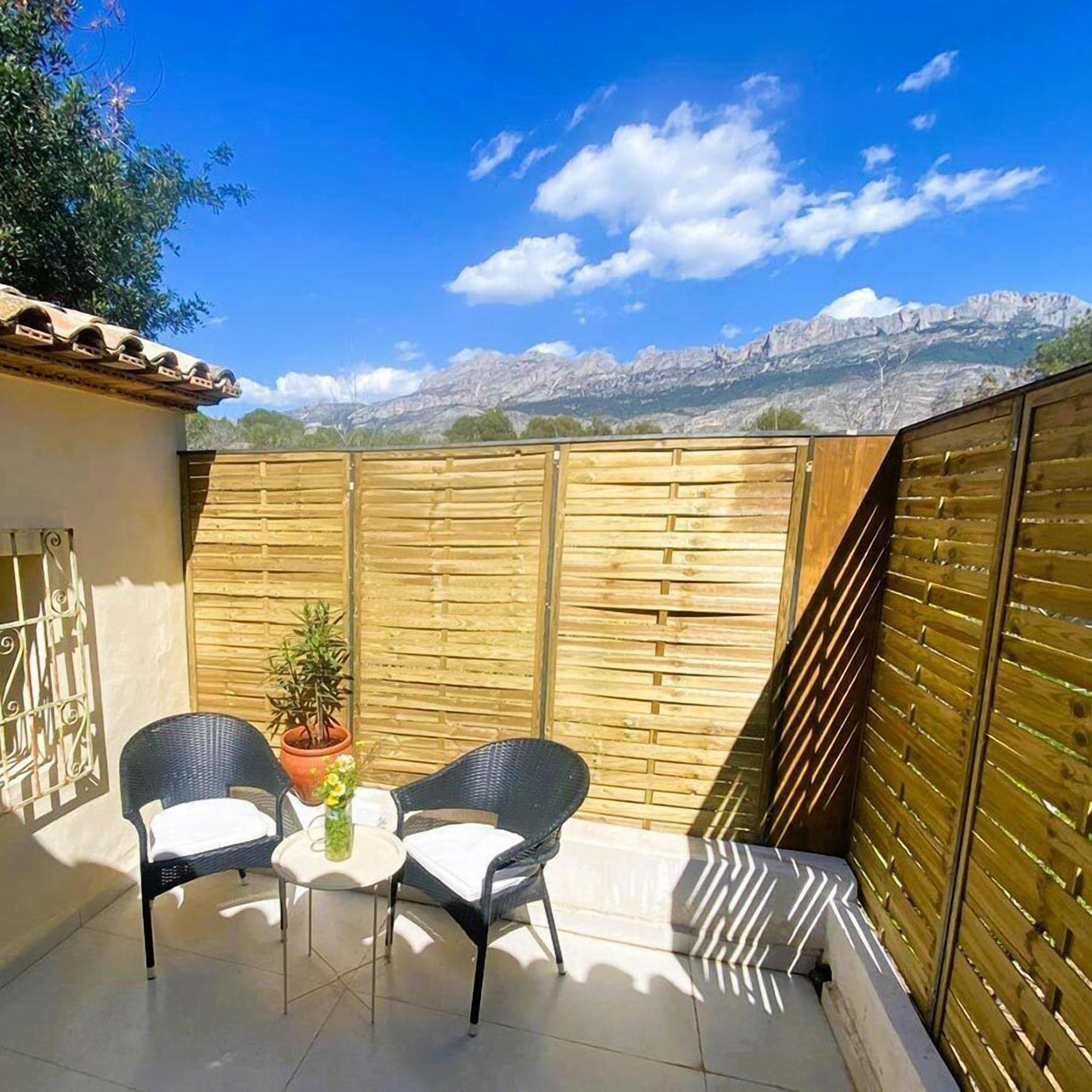 Un patio con dos sillas, una mesa, una planta en maceta y vistas a montañas.