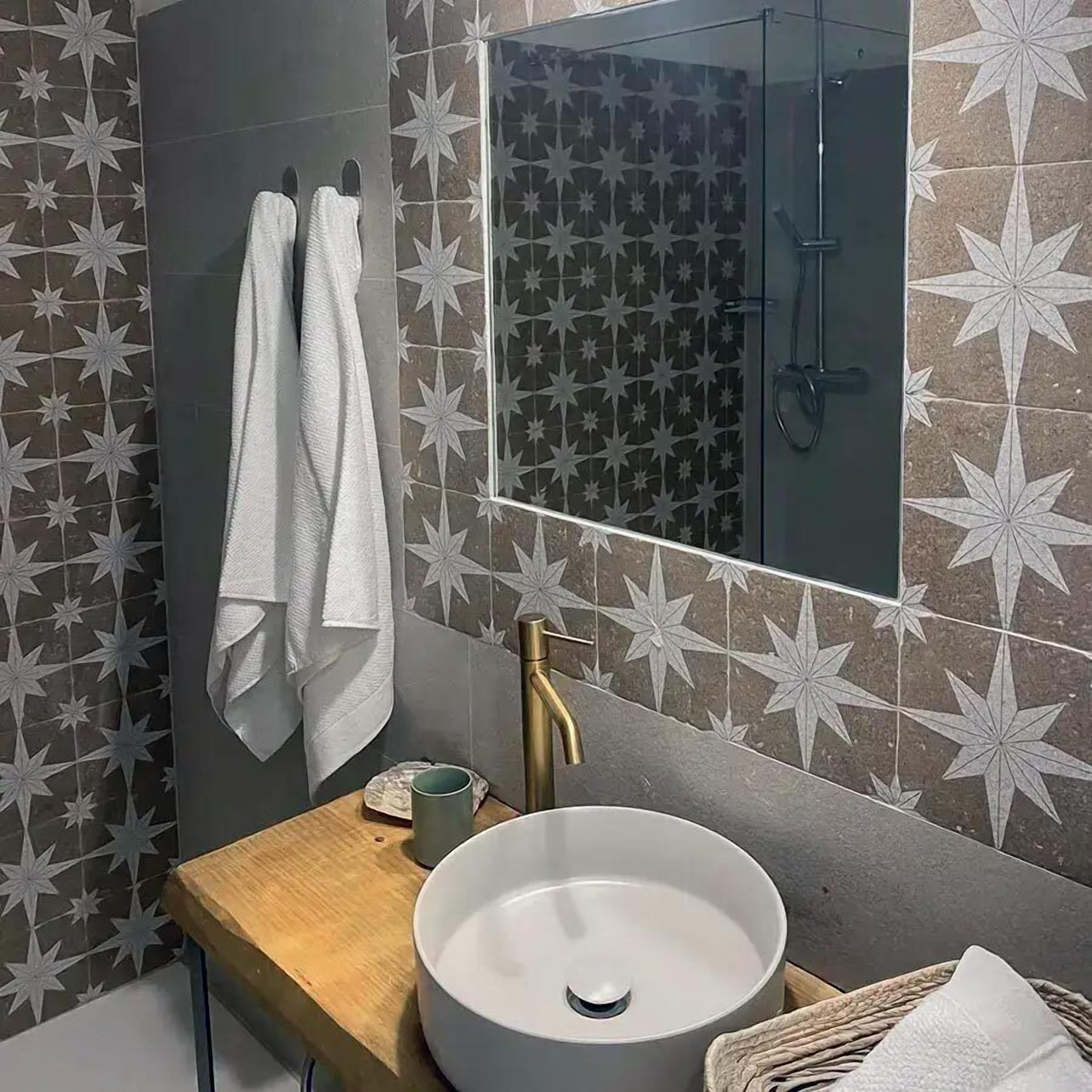 Un baño con pared de azulejos estampados de estrellas, un lavamanos con grifo dorado y un espejo encima.