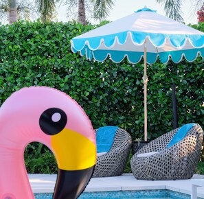 Ein Poolbereich mit Schwimmreifen in Flamingo-Form, Liegestühlen und einem blau-weißen Sonnenschirm.
