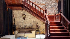A grand staircase with wooden balusters leading to a stone wall. A sofa and a coffee table are positioned in the foreground.