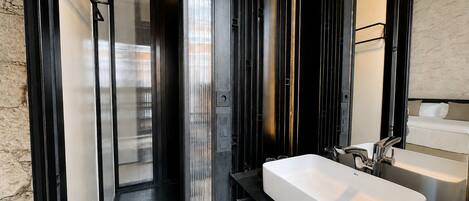 A modern bathroom with a large white sink, black shelves, and a glass door leading to a shower area.
