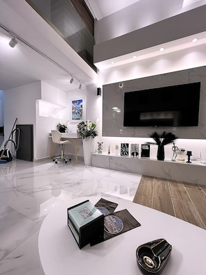 Ein modernes Wohnzimmer mit Flachbildfernseher, Couchtisch, Sofa und einer Essecke mit Stuhl und Tisch.