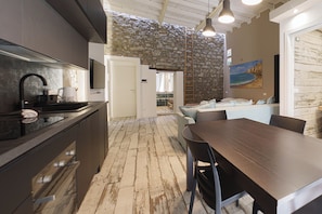 A modern kitchen with a stone wall, a dining area with a wooden table, and a living space with a sofa. - Cocciu D'Amuri loft by Wonderful Italy (Cefalù)