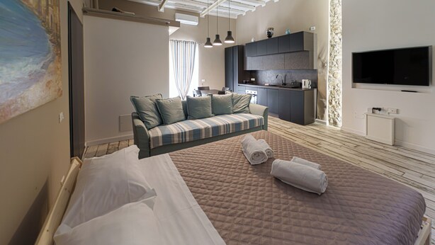 Una habitación de hotel moderna con una cama grande, un sofá, una cocina y un televisor montado en la pared.