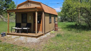 Een klein houten huisje met een veranda, twee stoelen, een tafel en een propaantank.