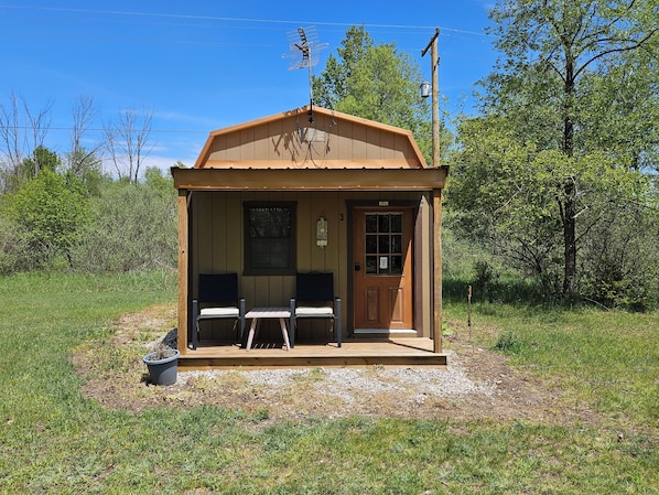 Eine kleine Holzhütte mit Veranda, zwei Stühlen, einem Tisch und einer Tür.