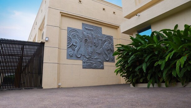 A building with a beige facade, a black metal gate, and a large green plant in the foreground.