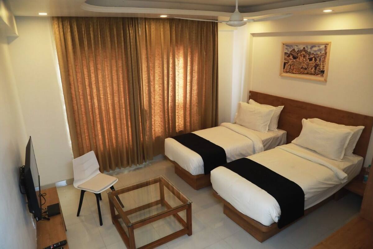 A hotel room with two beds, a television, a chair, and a small table.