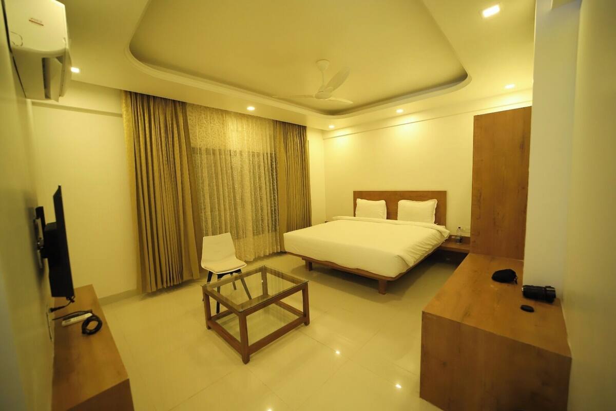 A hotel room with a bed, a glass table, a chair, a TV, and a wooden nightstand.