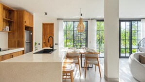 A modern kitchen with wooden cabinets, a central island, and a dining area with chairs and a table. - Villa Vista (Ubud)