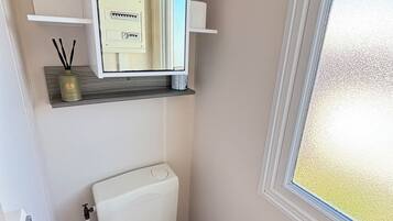Een kleine badkamer met toilet, spiegel, raam en een plank met toiletartikelen.