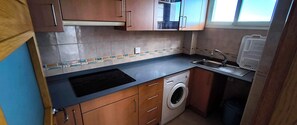 A compact kitchen with a built-in washing machine, a sink, and wooden cabinets. - Apartment with pool and terrace near the beach - Costa Blanca (Guardamar del Segura)
