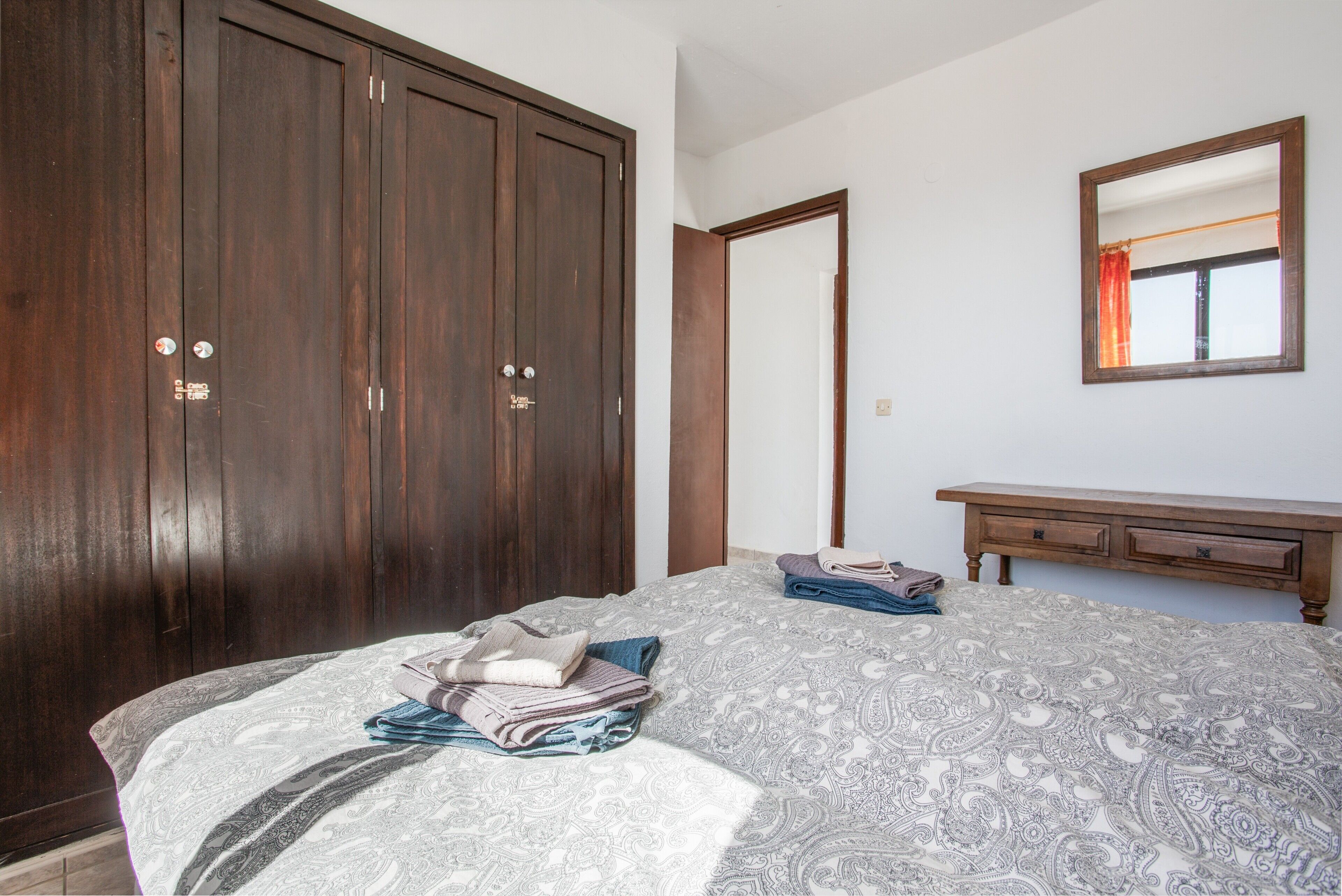 Un dormitorio con un armario grande, una cama con ropa de cama estampada, una mesita de noche y un espejo en la pared.