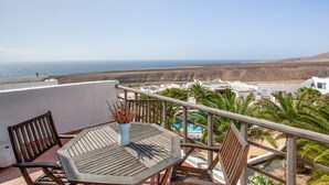 A balcony with a wooden table and chairs, overlooking a beach and a pool area. - Apartment in a Natural Park on Fuerteventura’s West Coast (Valle de Santa Inés)