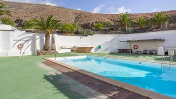 Une piscine avec une terrasse en bois, des palmiers et un mur blanc orné d’une bouée de sauvetage.