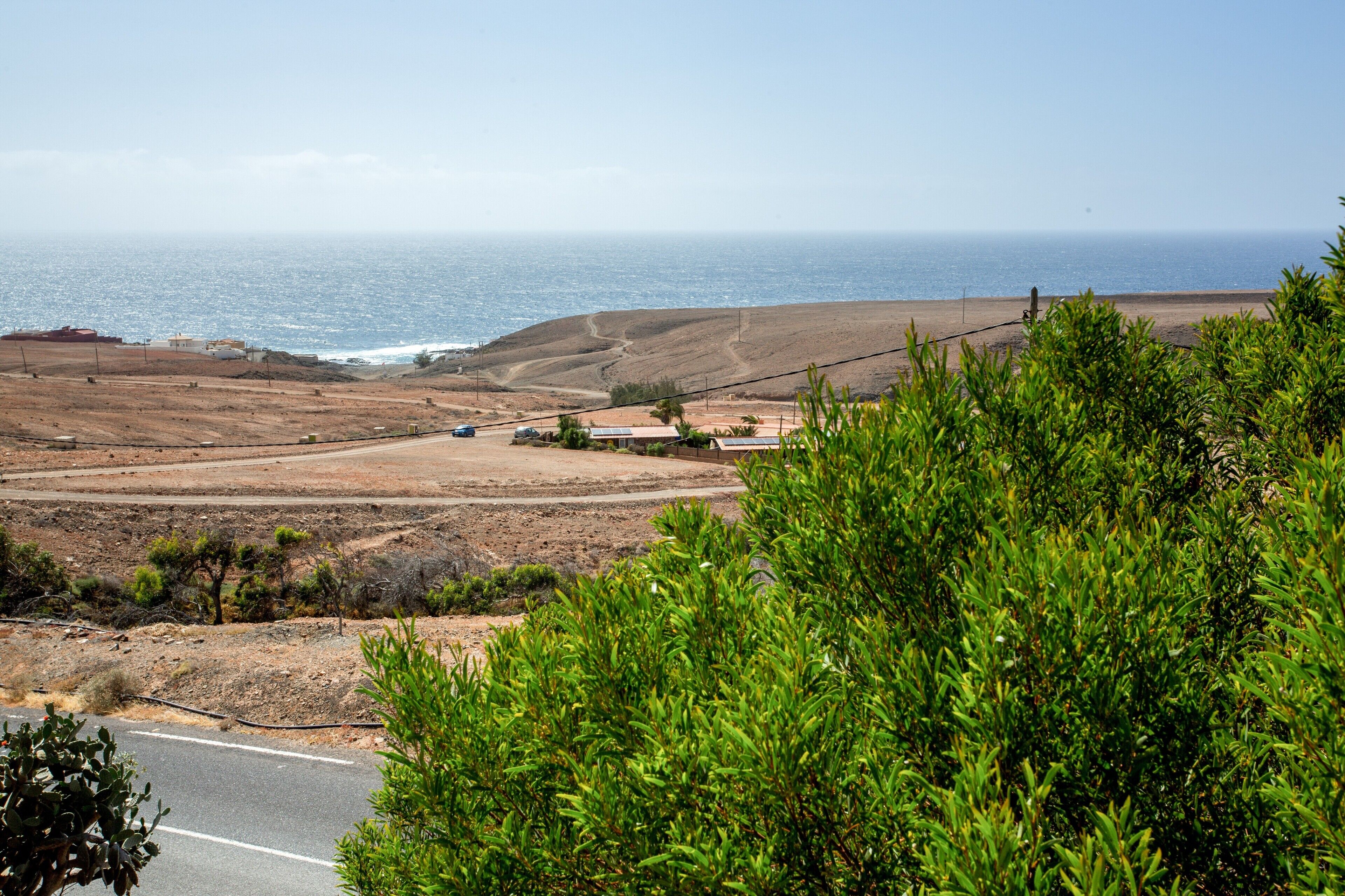 A coastal landscape with a road, sparse vegetation, and a distant view of the ocean.