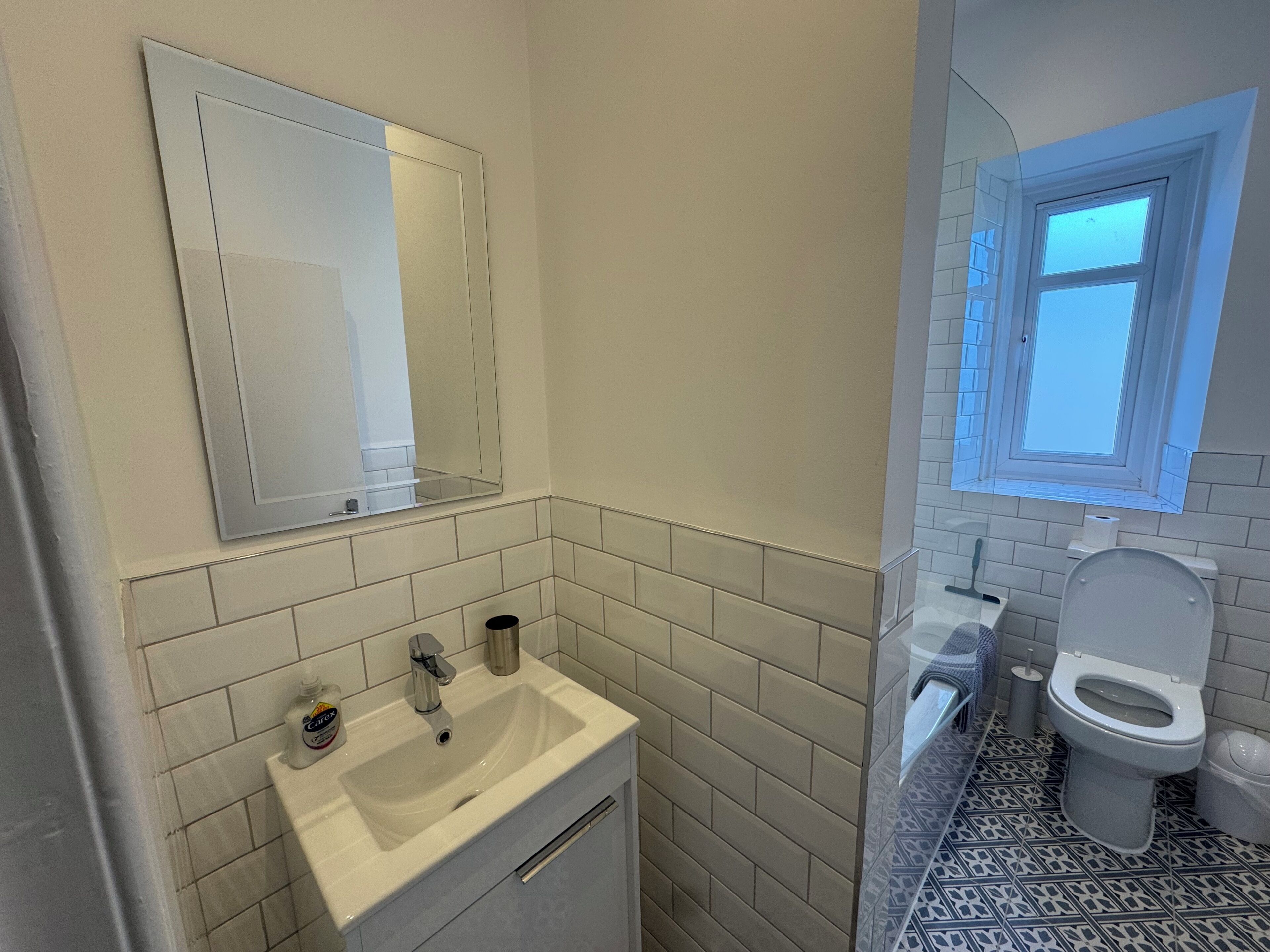 A bathroom with a white sink, a mirror, a toilet, and a window.