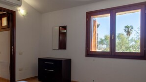 Ein Schlafzimmer mit Bett, Schminktisch, Spiegel und Fenster mit Blick auf Palmen.
