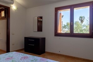 Ein Schlafzimmer mit Bett, Schminktisch, Spiegel und Fenster mit Blick auf Palmen.