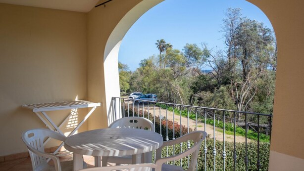 Ein Balkon mit Tisch und Stühlen, Blick auf Bäume und eine Straße.