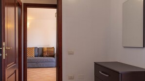 Ein Zimmer mit Holztür, einer Couch mit Kissen, einem Schrank und einem an der Wand befestigten Spiegel.