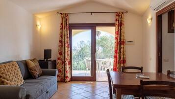 Una habitación con un sofá, una mesa de comedor con sillas, un televisor y un ventanal corredizo que da a un espacio exterior.