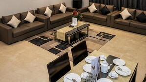 A modern living room with a dining area, featuring sofas, a coffee table, and a dining table set for four. - RURU TOWER (Manama)