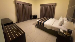 A hotel room with a bed, bedside table, lamp, curtains, and a small nightstand. - RURU TOWER (Manama)
