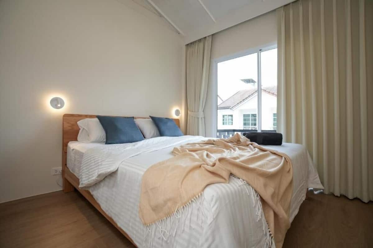 A bedroom with a bed, a window with curtains, and a wall-mounted light.