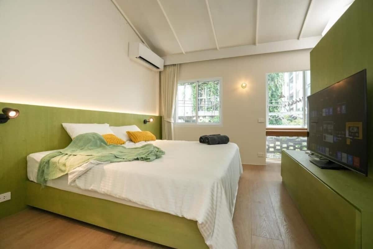A bedroom with a bed, a TV, a window, and an air conditioning unit.
