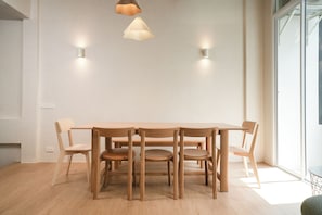 A dining area with a wooden table and chairs, pendant lighting, and wall sconces. - dayonespace (Bangkok)