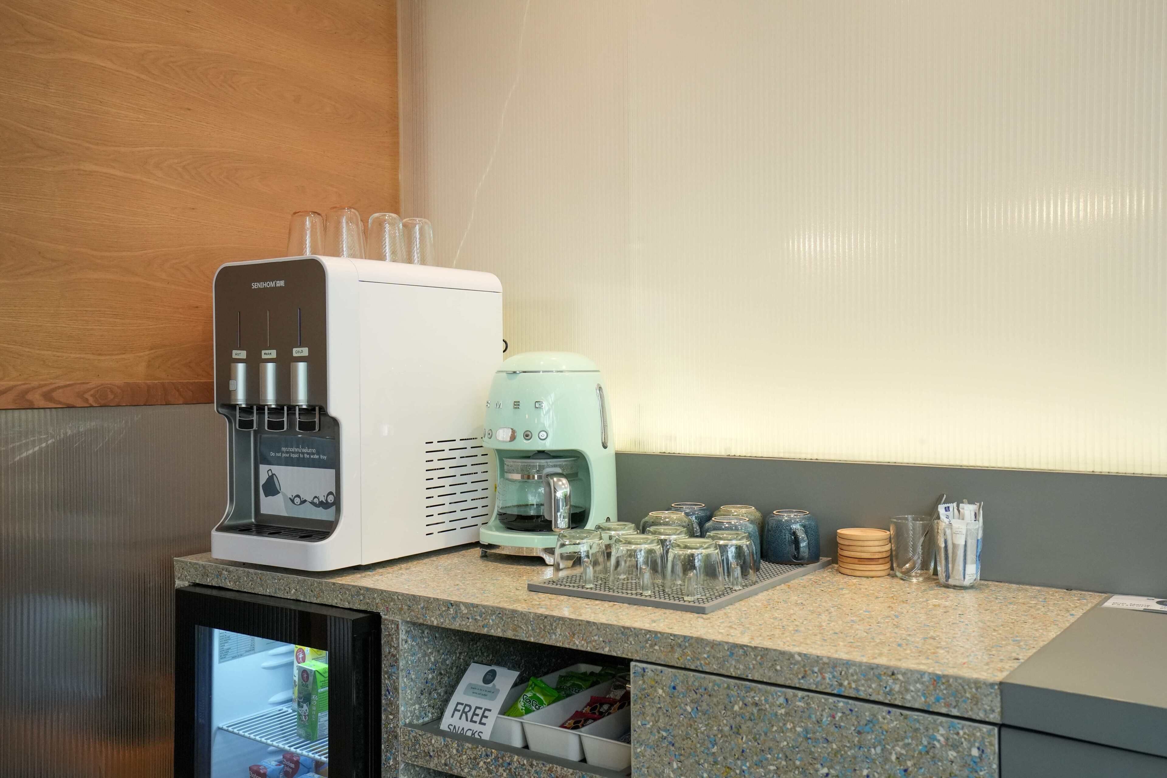 A kitchenette with a coffee maker, a water dispenser, and a refrigerator.
