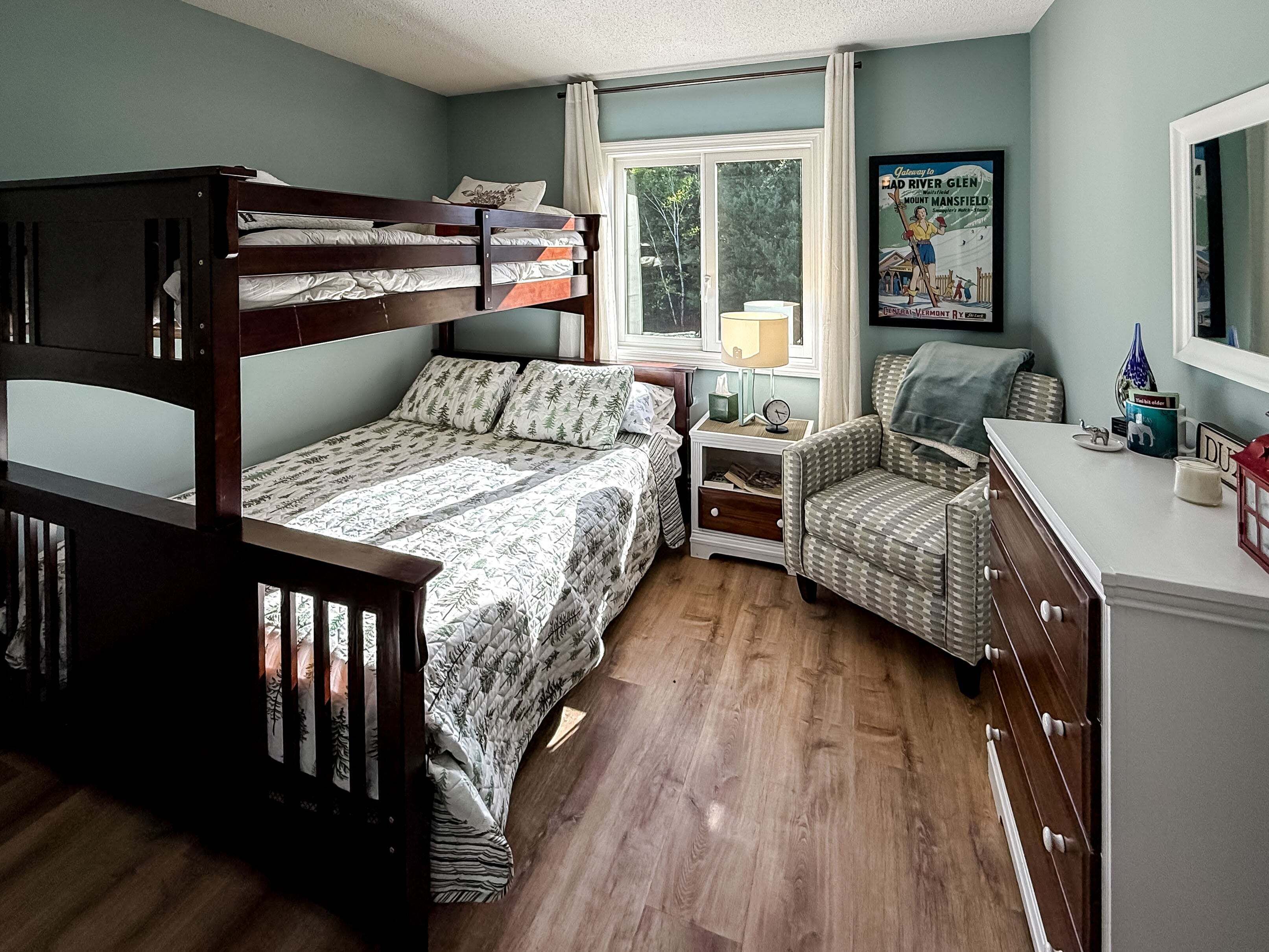A bedroom with a bunk bed, a single bed, a chair, a nightstand, a dresser, a window, and a poster on the wall.