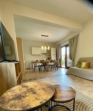 Ein modernes Wohnzimmer mit einer Couch, einem Essbereich mit Stühlen, einer Küche mit Schränken und einem Fernseher auf einem Schrank.